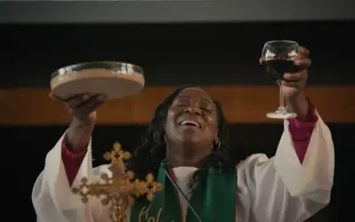 Une femme, peut-être une marraine de substitution, célèbre la communion en levant une coupe de vin et une patène.