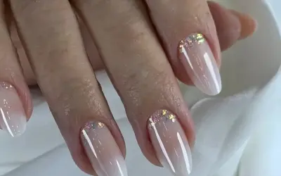 Eleganckie paznokcie w stylu babyboomer z subtelnym brokatem. Delikatny gradient od cielistego różu do bieli, ozdobiony iskrzącymi drobinkami.