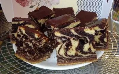 Wilgotne ciasto zebra z polewą czekoladową, pokrojone na kwadratowe kawałki, prezentuje się apetycznie na białym talerzu.