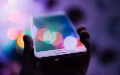 Dłoń trzyma telefon z kolorowymi światłami na ekranie. Chcesz wiedzieć, jak zrobić zdjęcie z filmu na telefonie?