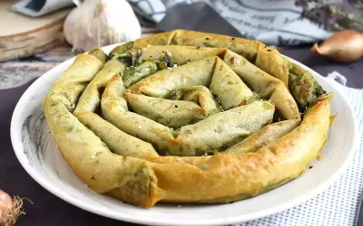 Złocisty borek ze szpinakiem, zwinięty w spiralę, prezentuje się apetycznie na białym talerzu. W tle czosnek i cebulka.