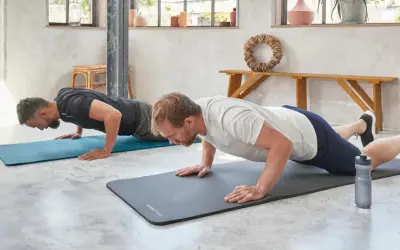 Dwóch mężczyzn wykonuje ćwiczenia na triceps w domu, robiąc pompki na matach.
