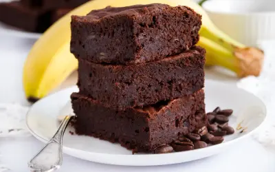 Stos puszystych brownie z bananami, ozdobiony ziarnami kawy, na talerzu z bananem w tle.