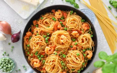 Linguine mit Garnelen und Erbsen in einer cremigen Tomatensauce, garniert mit frischem Basilikum.