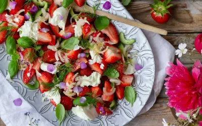 En härlig somrig sallad med jordgubbar, mozzarella, gurka och färska örter, dekorerad med ätbara blommor.
