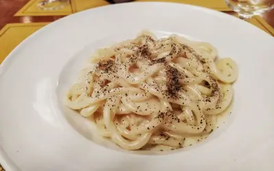 Piatto di pici cacio e pepe, pasta fresca condita con pecorino romano e pepe nero macinato fresco, servita su un piatto bianco.