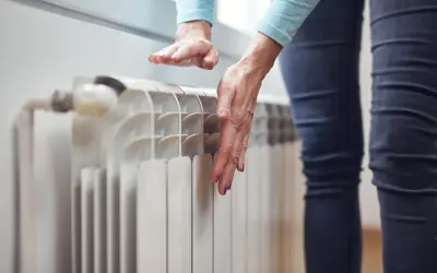 Dłonie sprawdzają temperaturę grzejnika, zastanawiając się, dlaczego grzejnik jest zimny na dole.