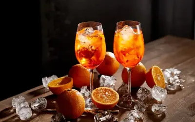 Dwa kieliszki Aperol Spritz, pomarańcze i lód na drewnianym stole. Aperol co to? Orzeźwiający drink na lato.
