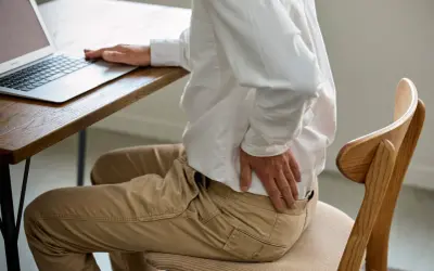 Homme assis à un bureau, se tenant le bas du dos. Il se demande combien de temps d'arrêt pour une discopathie.