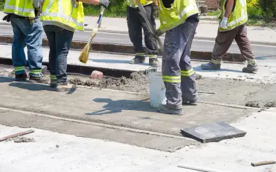 Prace interwencyjne: robotnicy w kamizelkach odblaskowych wylewają beton na torowisko.