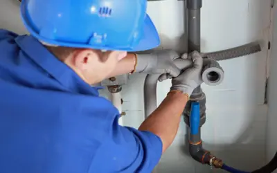 Instalator w niebieskim kasku i rękawiczkach montuje rury, pokazując, jak zrobić odpowietrzenie szamba.