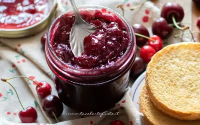 Un barattolo pieno di deliziosa marmellata di ciliegie, pronto per essere spalmato su fette biscottate.