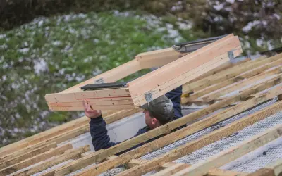 Pracownik montuje drewnianą ramę okna dachowego na konstrukcji dachu. To kluczowy etap, jak zamontować okno dachowe.