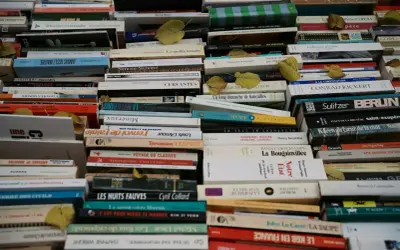 Une pile de livres anciens, certains jaunis par le temps. On peut y lire des titres comme "La nuit à Paris" ou "Le savoir-vivre libertin". L'image invite à interagir avec la conjugaison des mots et des histoires.