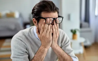 Mann mit Brille reibt sich die Augen, wirkt gestresst. Manche glauben, rauchen hilft gegen Stress, doch das ist ein Trugschluss.