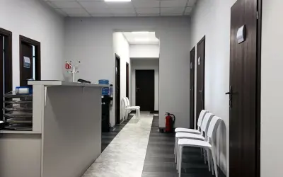 Korytarz przychodni z recepcją, drzwiami i białymi krzesłami.