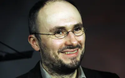 Uśmiechnięty mężczyzna w okularach, z zarostem. Sebastian Krajewski, którego życie prywatne budzi zainteresowanie, wygląda na zrelaksowanego.