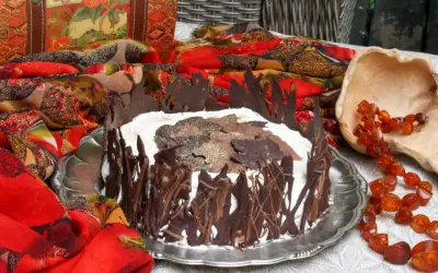 A chocolate-decorated cake with whipped cream and chocolate leaves on top, set on a silver platter.