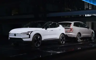 Dwa białe, nowe Volvo na czarnej scenie. Jedno z przodu z charakterystycznymi światłami, drugie z tyłu z nowoczesnymi lampami.