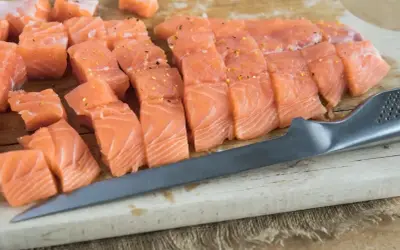 Świeży, pokrojony w kostkę i plastry łosoś, idealny jako jaki łosoś do sushi, leży na desce obok noża.