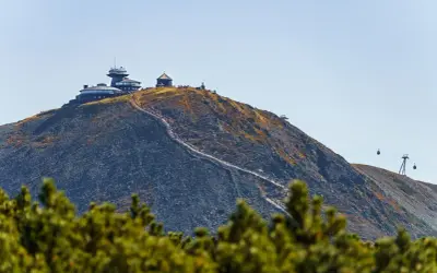 Szczyt Śnieżki w Karkonoszach, z obserwatorium i schroniskiem, po którym wije się ścieżka turystów. W tle kolejka linowa.