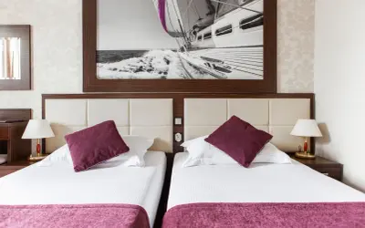 Dwie wygodne łóżka w pokoju hotelowym, nad nimi obraz z żaglówką. Idealne miejsce na wypoczynek, jak sugerują primavera jastrzębia góra opinie.