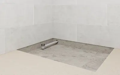 Installation d'un receveur de douche : un siphon est posé sur une chape avant le carrelage.