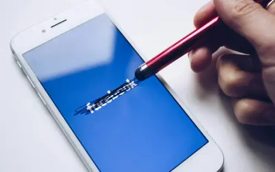 Dłoń z rysikiem próbuje sprawdzić, jak sprawdzić ile zostało blokady na FB, dotykając ekranu telefonu z logo Facebooka.