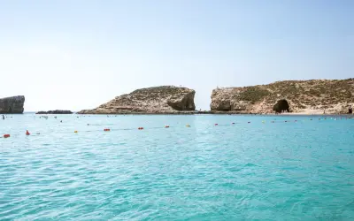 Turkusowa woda, skaliste klify i plaża z ludźmi. Idealne miejsce na wakacje, zastanawiasz się, ile leci się na Maltę?