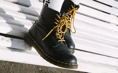 Schwarze Dr. Martens mit gelben Schnürsenkeln auf einer weißen Bank. Sie fallen eher groß aus, also lieber eine Nummer kleiner wählen.