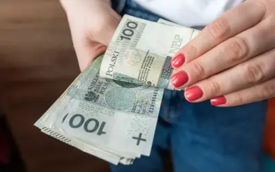 Dłonie z czerwonymi paznokciami trzymają stos banknotów 100 zł. To polska stopa referencyjna NBP.