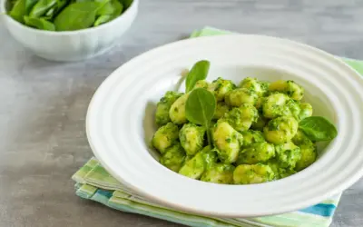 Puszyste gnocchi z pesto, podane w białej misce, ozdobione świeżymi listkami szpinaku. Obok miseczka ze świeżym szpinakiem.