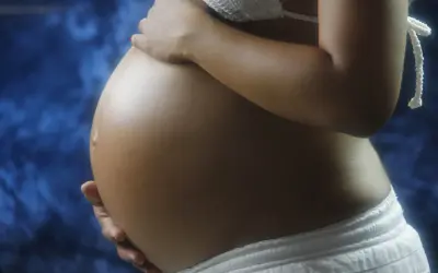 Pancia di donna incinta, con mani che la accarezzano. Si intravede un bikini bianco e uno sfondo blu. L'addome è tonico, forse con un leggero intestino iperecogeno visibile.