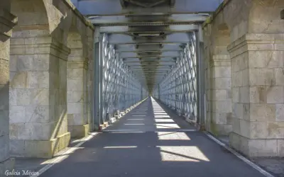 El **puente internacional Tui** se alza imponente, un túnel de metal y piedra que se pierde en la distancia, proyectando sombras geométricas sobre el asfalto.