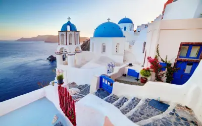 Białe domy z niebieskimi kopułami kościołów na tle morza i wysp. Widok na kaldera Santorini o zachodzie słońca.