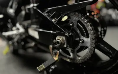 Zbliżenie na tylne koło motocykla z widocznym łańcuchem i zębatką. Pokazuje elementy potrzebne do tego, jak rozkuć łańcuch motocyklowy.