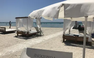 Beach cabanas with white curtains and beds on a sandy beach with the ocean in the background.