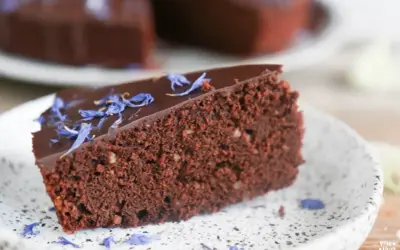 Ein Stück saftiger schokokuchen ohne zucker, garniert mit blauen Kornblumenblättern auf einem Teller.