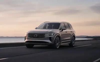 Elegancki Volvo XC90 T8 w kolorze szarym jedzie wzdłuż malowniczego wybrzeża o zachodzie słońca.