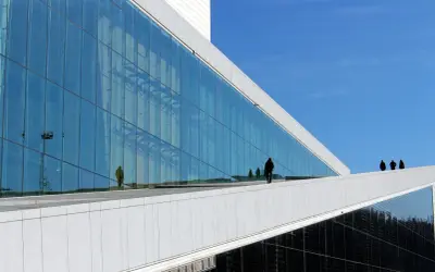 Nowoczesna architektura Uniwersytetu w Oslo z lustrzaną fasadą odbijającą niebo i ludzi.