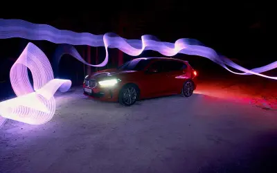 Czerwony samochód w nocnej scenerii, otoczony fioletowymi i różowymi smugami światła, efekt **panning**.