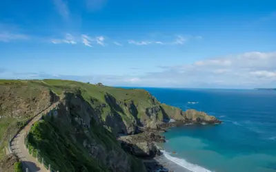 Chemin côtier verdoyant sur les falaises de Jersey, idéal pour visiter Jersey à pied. Mer bleue et ciel clair.