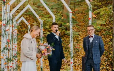 Piękna panna młoda z bukietem, pan młody przemawia do mikrofonu, a pan młody z uśmiechem. Wesele jesienią w otoczeniu kolorowych liści.