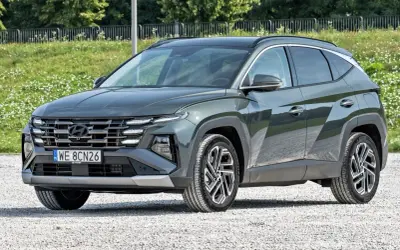Nowy, tani SUV Hyundai Tucson w ciemnozielonym kolorze, zaparkowany na żwirowej drodze.