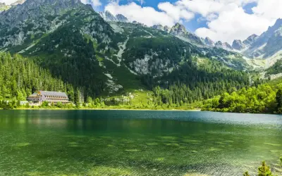 Zielone jeziora w Tatrach, otoczone lasem i majestatycznymi szczytami, z widocznym hotelem nad brzegiem.