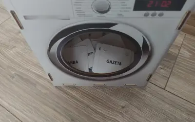 Kartonowa pralka z bębnem pełnym kart z napisami "GAZETA", "ZKA", "ARBA".