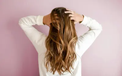 Mujer con pelos largos y ondulados, de color castaño, jugando con su cabello.