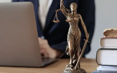 Justitia-Statue neben Laptop und Büchern. Ein Anwalt prüft Unterlagen, vielleicht wegen eines Widerspruchs Pflegegrad.