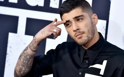 Zayn Malik, były członek One Direction, z tatuażami na ramieniu i palcami ozdobionymi pierścionkami, dotyka czoła.