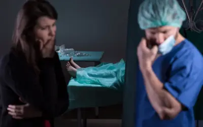 Smutna kobieta i lekarz w masce, obok zakryte ciało na stole. Kiedy sekcja jest obowiązkowa, emocje biorą górę.
